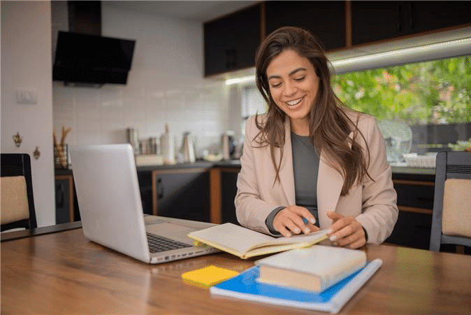 smiling woman at a desk reading a book, with a computer