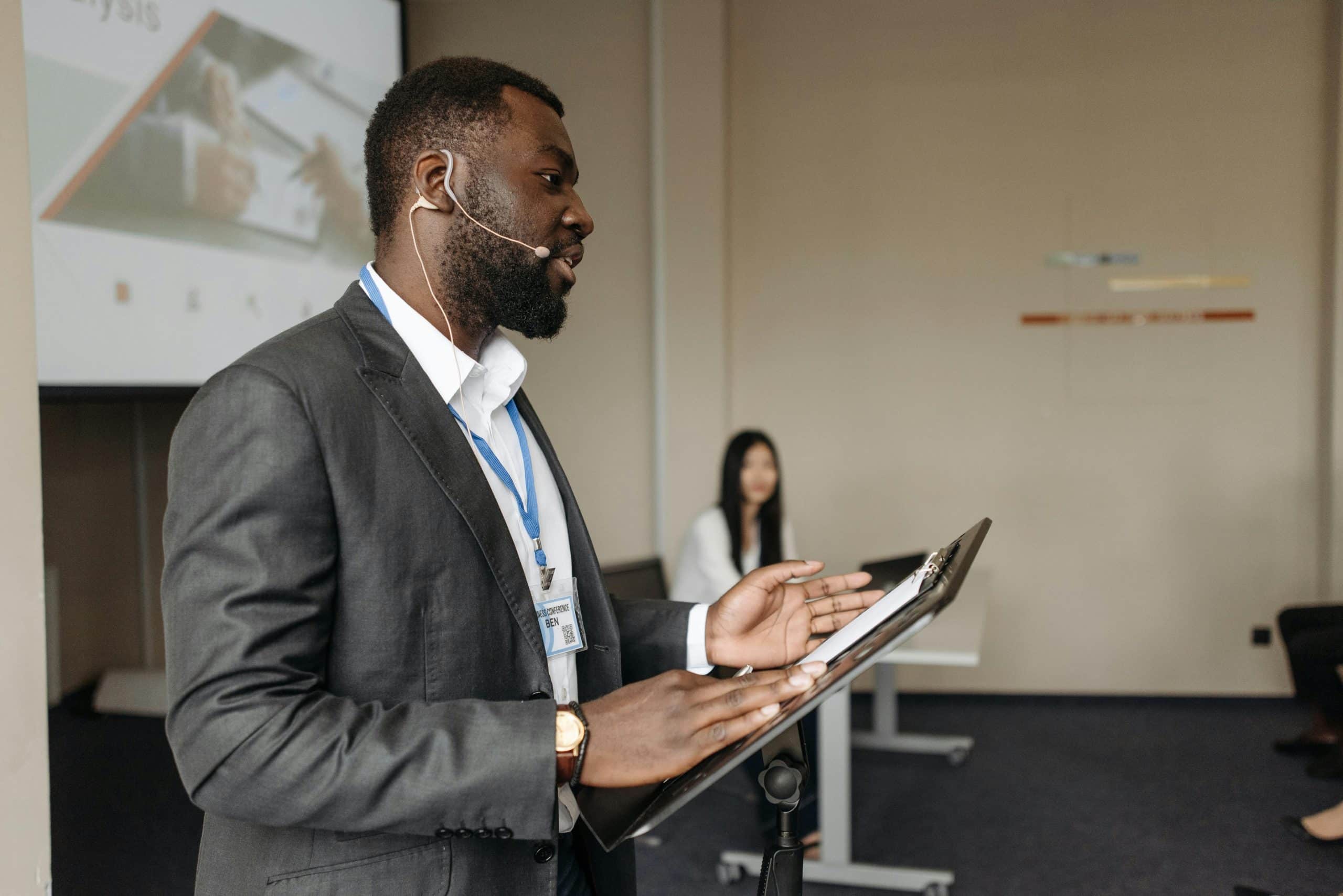 man lectures to a classroom while teaching assistant looks on